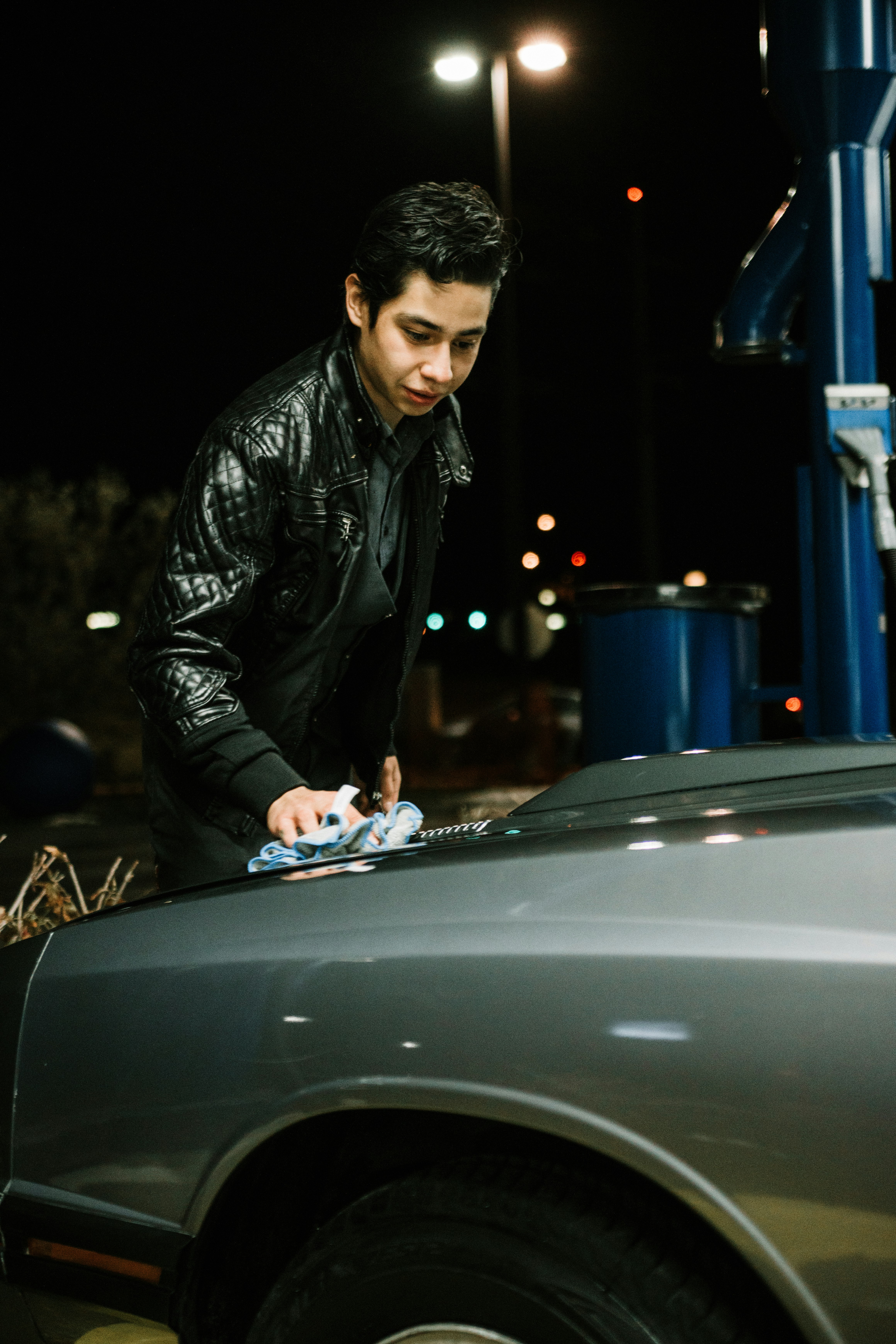 man in black leather jacket leaning on black car